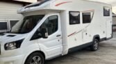Obytné auto, bílé s černými detaily, zaparkované na rovné ploše. Ideální pro dobrodružství na cestách.