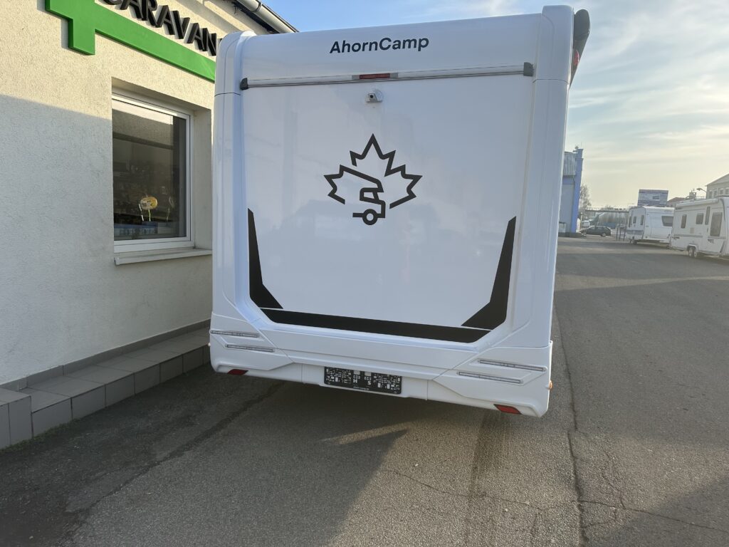 Zadní pohled na karavan AhornCamp, který stojí před prodejním stánkem. Vhodný pro dobrodružství.