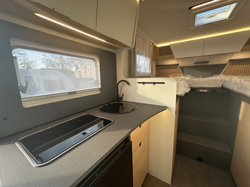 Interiér moderního karavanu s kuchyňským koutem a prostorným sezením. Elegantní design a dostatek světla.