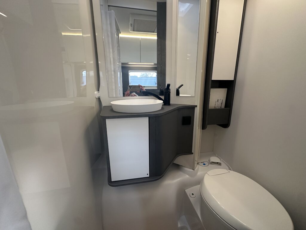 Obrázek interiéru obytného auta s moderním umyvadlem a toaletou, ideální pro pohodlné cestování.