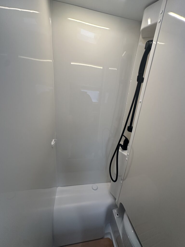 Obrázek zobrazuje sprchu v obytném autě, moderní a elegantní design pro maximální pohodlí na cestách.