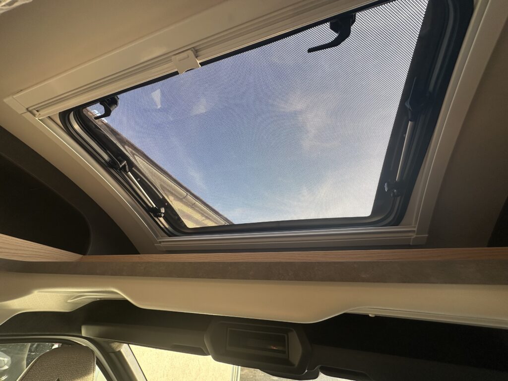 Obrázek interiéru obytného auta s oknem a krásným výhledem na modrou oblohu.