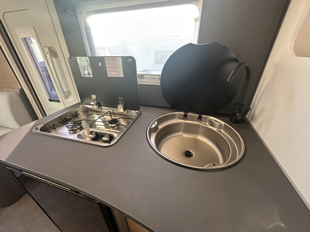 Moderní kuchyňka s dřezem a vařičem. Ideální pro obytné auto nebo karavan. Značka a model nejsou uvedeny.