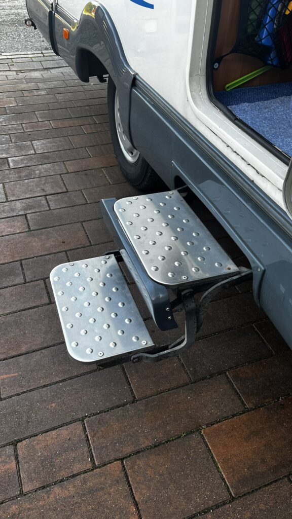 Obrázek ukazuje schody obytného auta, které usnadňují vstup do interiéru. Splňuje funkčnost a praktičnost.