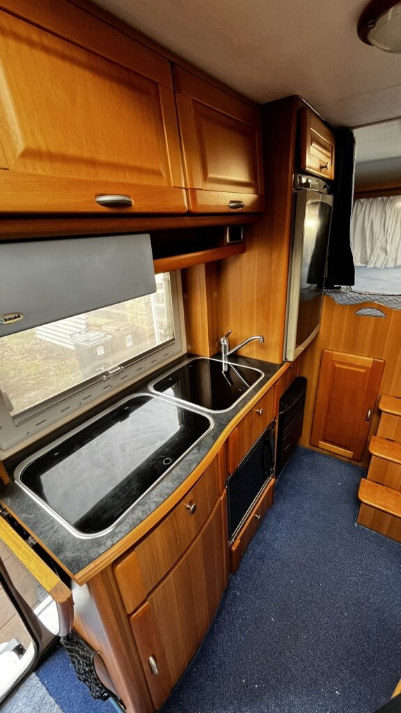 Interiér obytného vozu s dřevěným nábytkem a kuchyňským vybavením. Ideální pro pohodlné cestování.