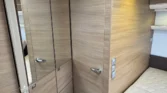 Obrázek interiéru obytného vozu, zaměřený na skříně a prostor na spaní, moderní design s dřevěnými prvky.