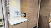 Obrázek interiéru obytného auta s dřevěnými skříňkami a moderními spotřebiči. Design jako Laika.