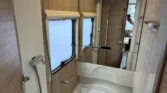 Koupelna v moderním obytném autě, zahrnující sprchu, zrcadlo a úložné prostory. Elegantní design s dřevěnými prvky.