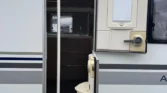 Obrázek zachycuje elegantní karavan s otevřenými dveřmi, připravený na dobrodružství.
