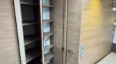 Obrázek interiéru obytného auta s úložným prostorem a manželskou postelí, moderní dřevěné prvky.