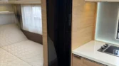 Obrázek interiéru moderního karavanu, který nabízí pohodlné spaní a vybavení pro vaření.
