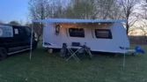 Na obrázku je karavan s venkovním posezením a osvětlením, ideální pro kempování.